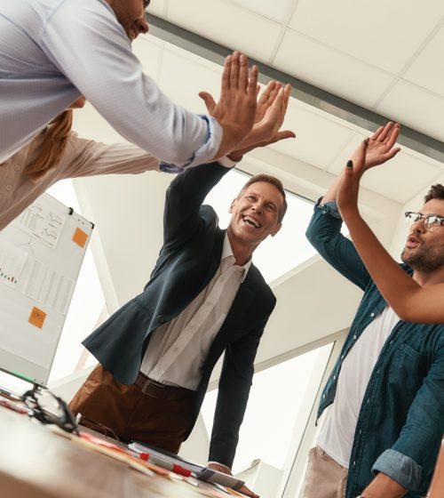 Success! Business people giving each other high-five and smiling while working together in the modern office. Teamwork