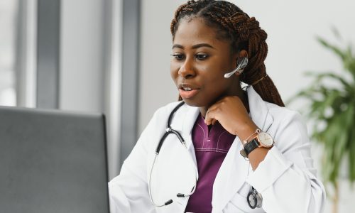 medicine, online service and healthcare concept - happy smiling african american female doctor or nurse with headset and laptop having conference or video call at hospital